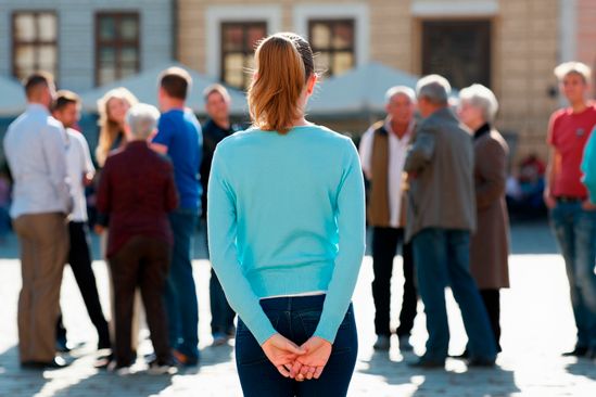 Женщина стоит у толпы и боится подойти